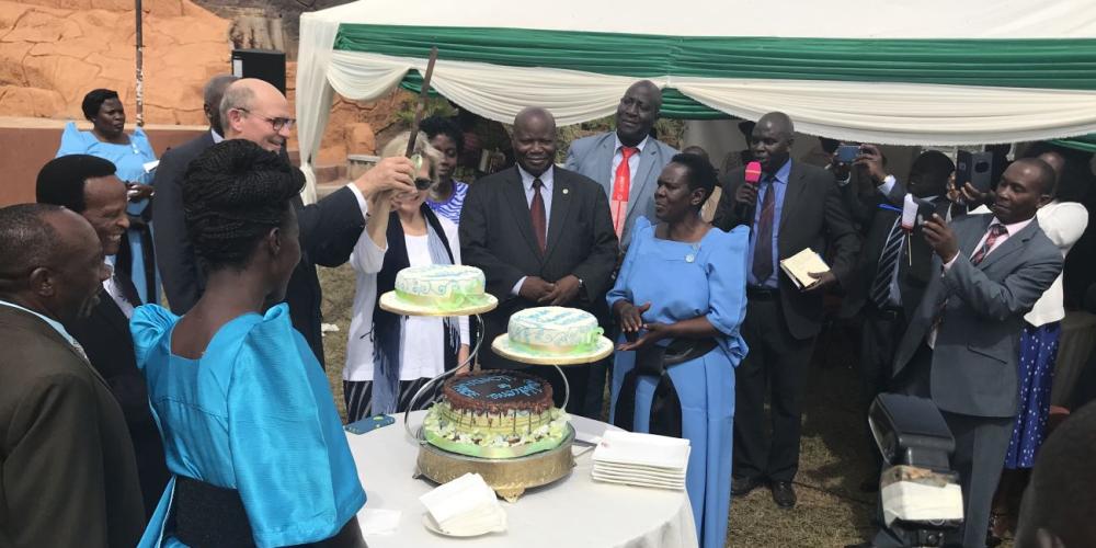 Adventist Church president Ted Wilson holding a knife high to cut cakes at a welcome reception on the grounds of Peniel Beach Hotel in Kampala, Uganda, on Feb. 14, 2018.  Local church leaders asked him to hold the knife like a sword. (Andrew McChesney / Adventist Mission)